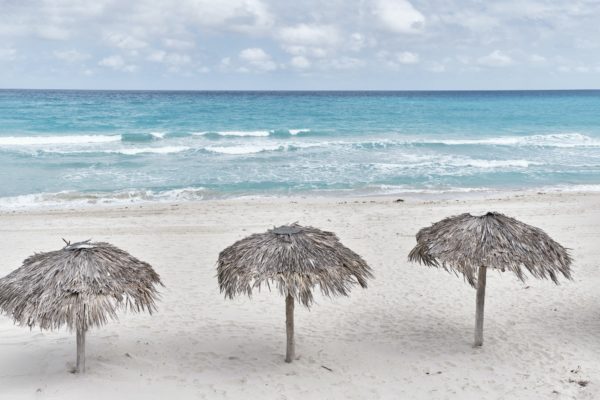 Atlantic sandy beach of Cuba, resort Varadero. Three palm leaf sun umbrellas