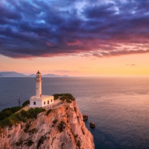 Lighthouse on the mountain peak at colorful sunset in summer